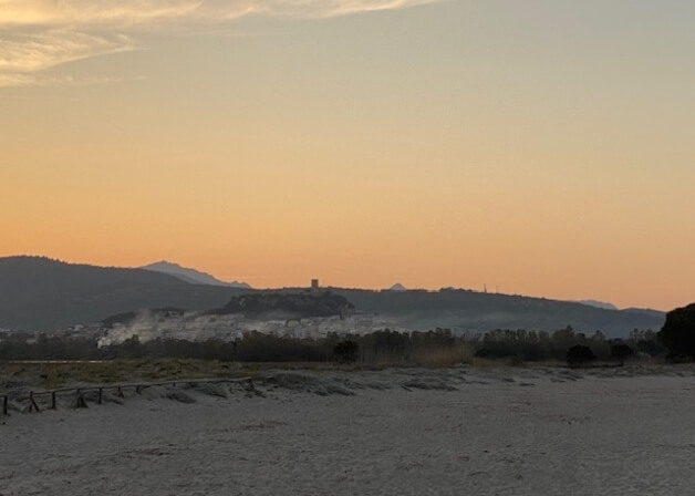 Spiaggia con recinzione, villaggio e colline al tramonto.