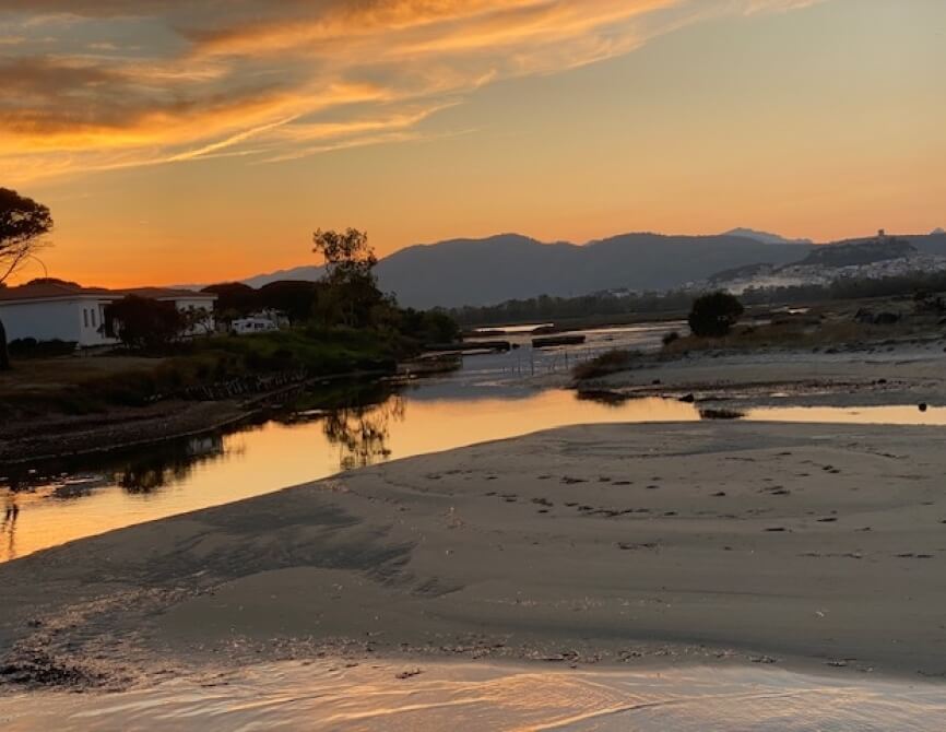 Fiume incontra l'oceano al tramonto, cielo arancione e giallo.