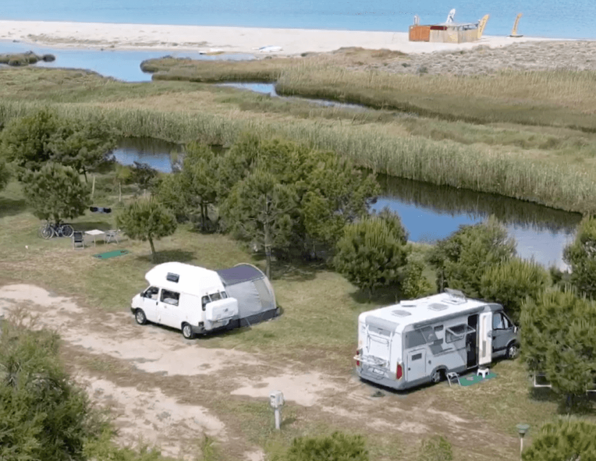 Due camper e una tenda in un'area erbosa vicino all'acqua.