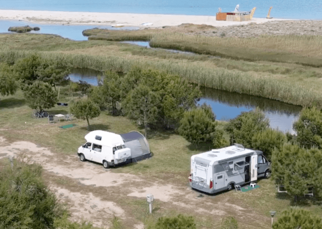 Due camper e una tenda su un'area erbosa vicino all'acqua.
