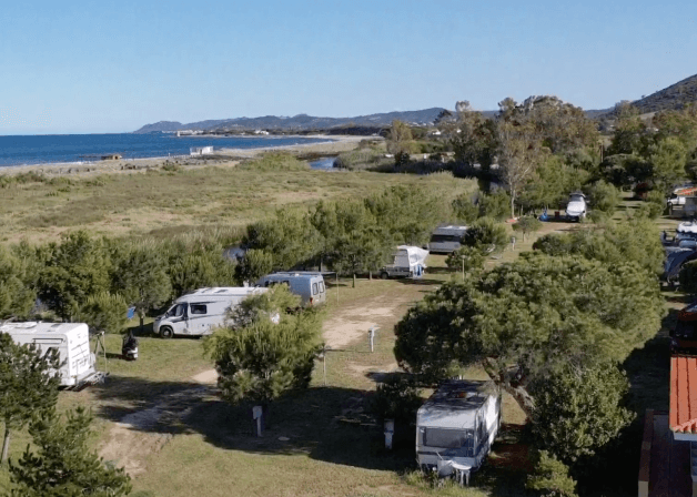 Campeggio con veicoli ricreativi, alberi e acqua sullo sfondo.