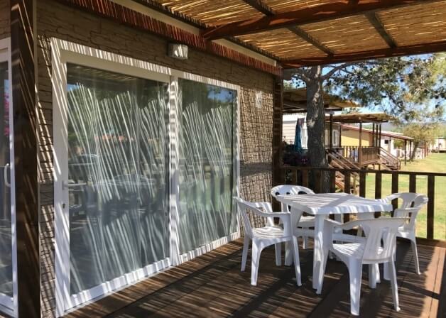 Patio con tavolo bianco, sedie, tetto in bambù e vegetazione.