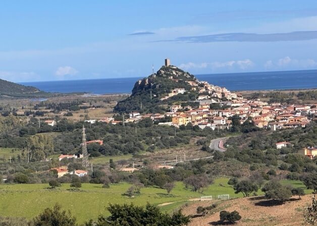 Città costiera su una collina con tetti arancioni e torre.