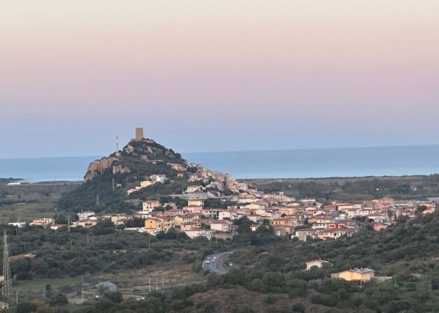 Città collinare con torri, tetti rossi e vista sul mare.