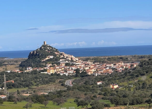 Città costiera con castello, colline verdi e mare sullo sfondo.