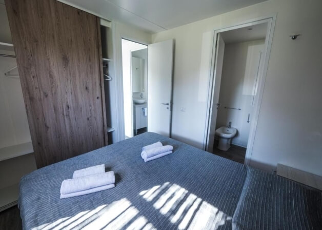 Letto con coperta grigia, asciugamani bianchi e armadio scuro.