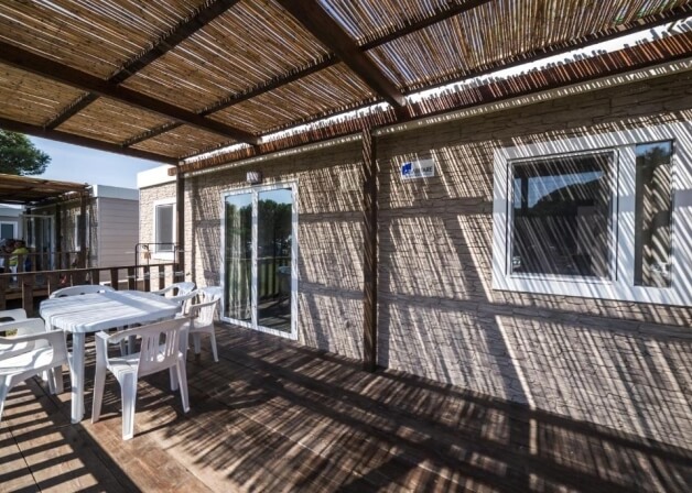 Deck with white table, chairs, thatched roof, and mobile home.