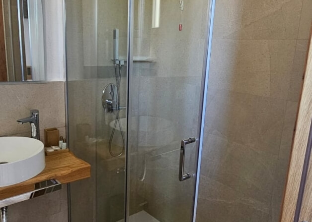 Bagno con doccia in vetro, lavabo rotondo e pareti chiare.