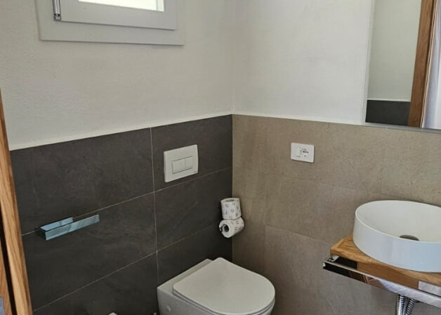 Bagno con WC, lavabo circolare, piastrelle grigie e tan.