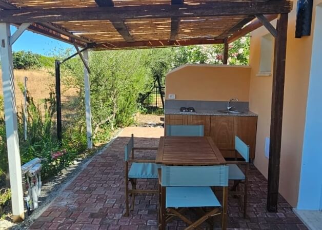 Cucina all'aperto con tavolo in legno e sedie blu.