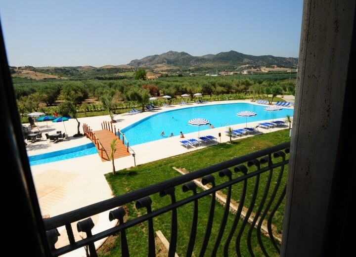 Immagine di una piscina rettangolare circondata da verde, con lettini e ombrelloni, in un ambiente sereno e tranquillo.