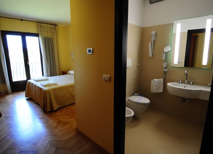 Camera con letto e bagno, pareti gialle, pavimento in parquet, bagno con lavabo, WC e bidet elettrico.