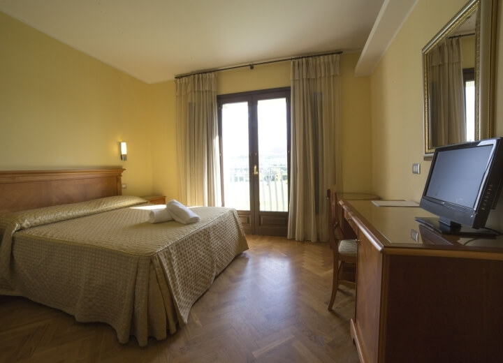 Camera d'hotel serena con letto beige, scrivania in legno, luce calda e decorazioni gialle che creano un'atmosfera tranquilla.