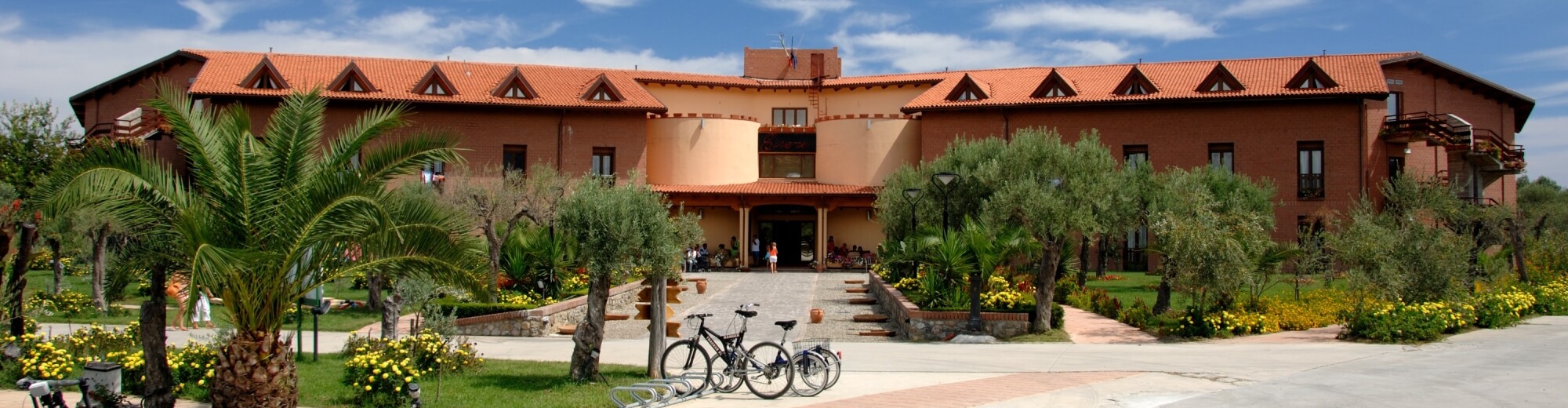 Immagine di un edificio marrone con tetto rosso, giardino fiorito, biciclette parcheggiate e un'atmosfera accogliente.