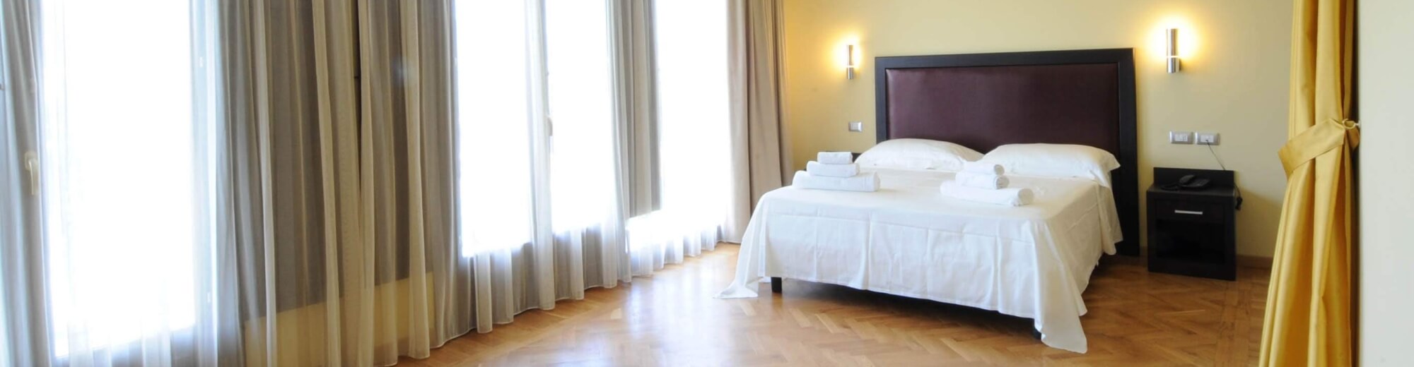 Camera d'albergo serena e ordinata, con decorazioni minimaliste, luce naturale e letto matrimoniale con lenzuola bianche.