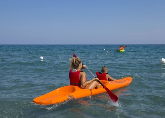 Tre persone in kayak nell'oceano calmo, una donna con giubbotto rosso e un bambino, mentre un'altra persona si avvicina.