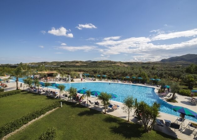 "Piscina all'aperto circondata da sedie a sdraio, ombrelloni e verde lussureggiante, con colline e montagne sullo sf