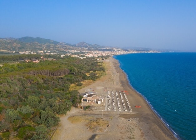 Spiaggia e città costiera vista da lontano, con alberi, barche arancioni e un'atmosfera calma e piacevole.