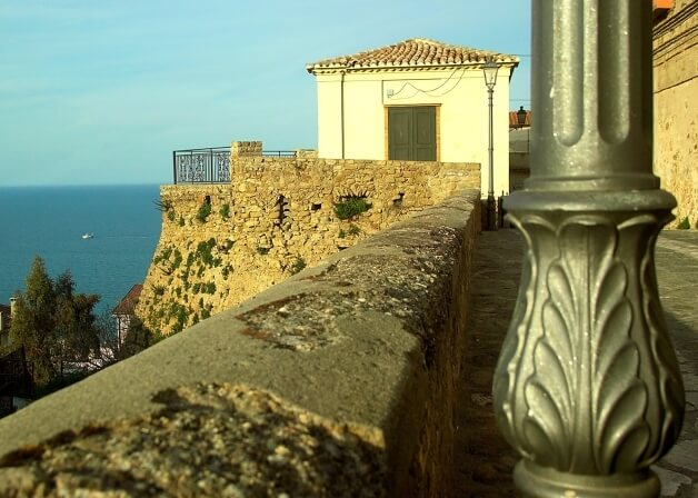 Scena costiera serena con un edificio bianco su una scogliera, vista sull'oceano e una barca che galleggia.