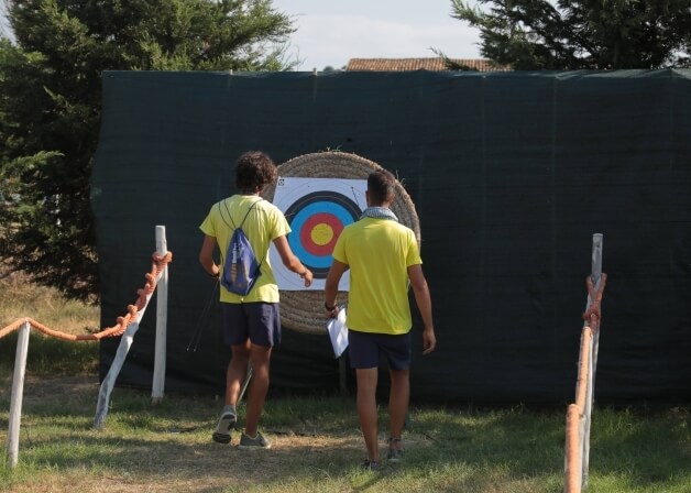 Due persone in abbigliamento sportivo davanti a un bersaglio colorato, con una barriera di corda in primo piano.