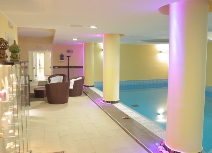 Area piscina interna serena con decorazioni moderne, pareti gialle, mobili eleganti e illuminazione soffusa.