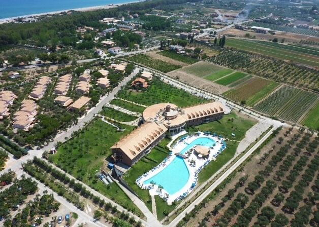 Vista aerea di un resort con piscine, giardini curati e paesaggio rustico, evocando lusso e relax in una giornata di sole.