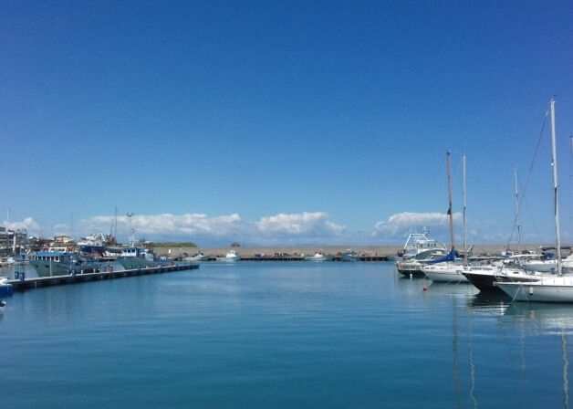 Una scena serena di un marina con cielo blu, acqua calma e barche ormeggiate lungo un lungo molo.