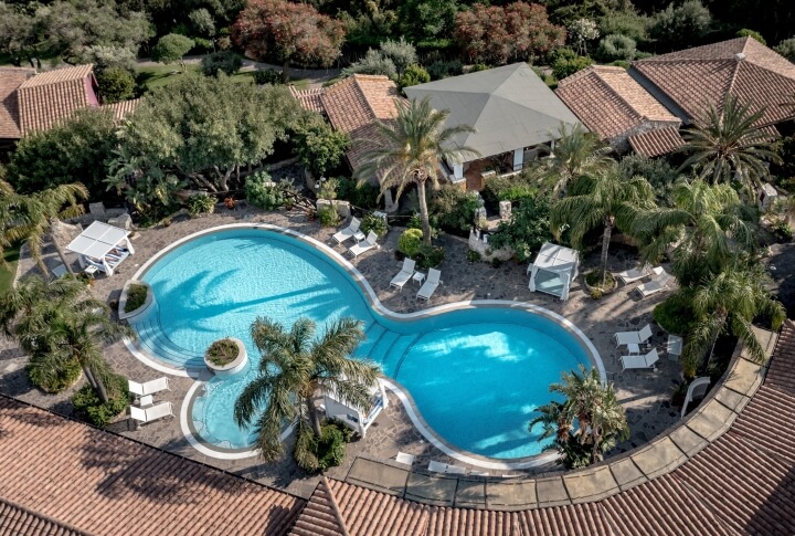 Vista dall’alto della piscina principale del Cruccùris Resort, immersa nel giardino mediterraneo. Area relax con bar adiacente e musica di sottofondo, pensata per un’atmosfera equilibrata e non invadente.