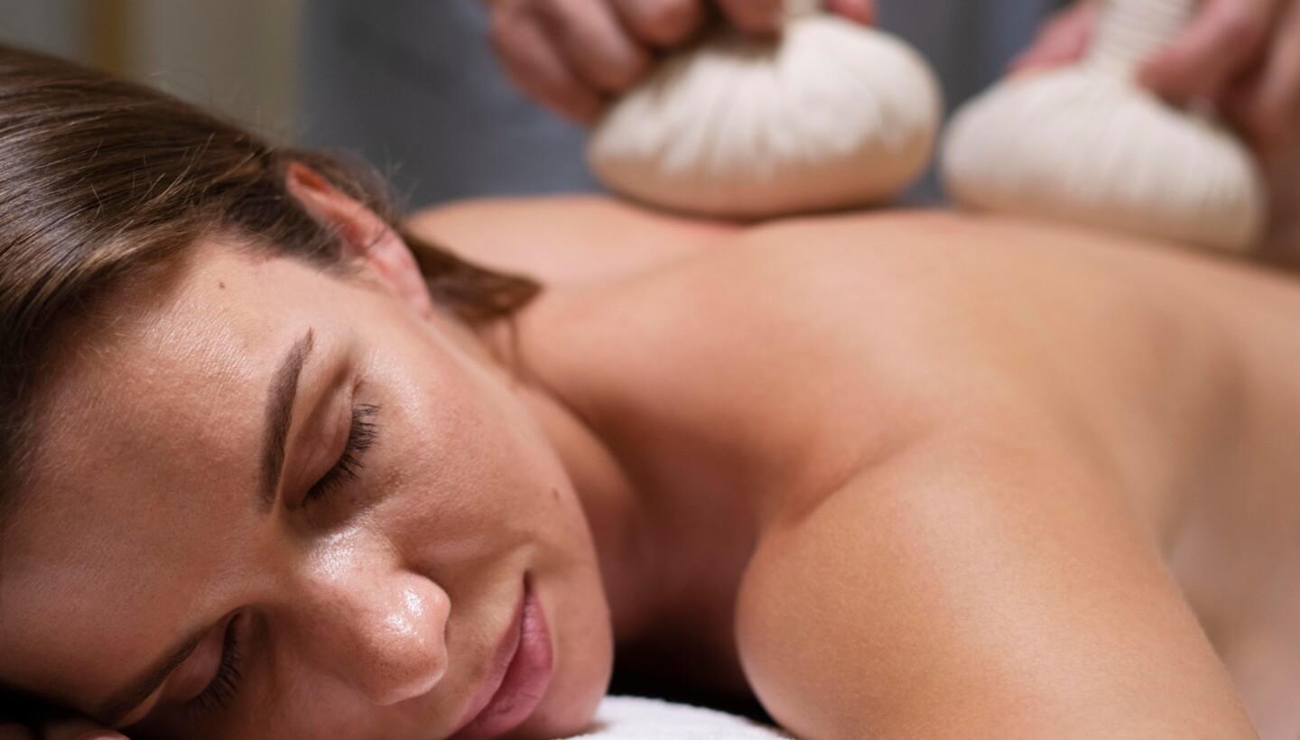 Donna sdraiata con gli occhi chiusi, massaggio con palline erboristiche.