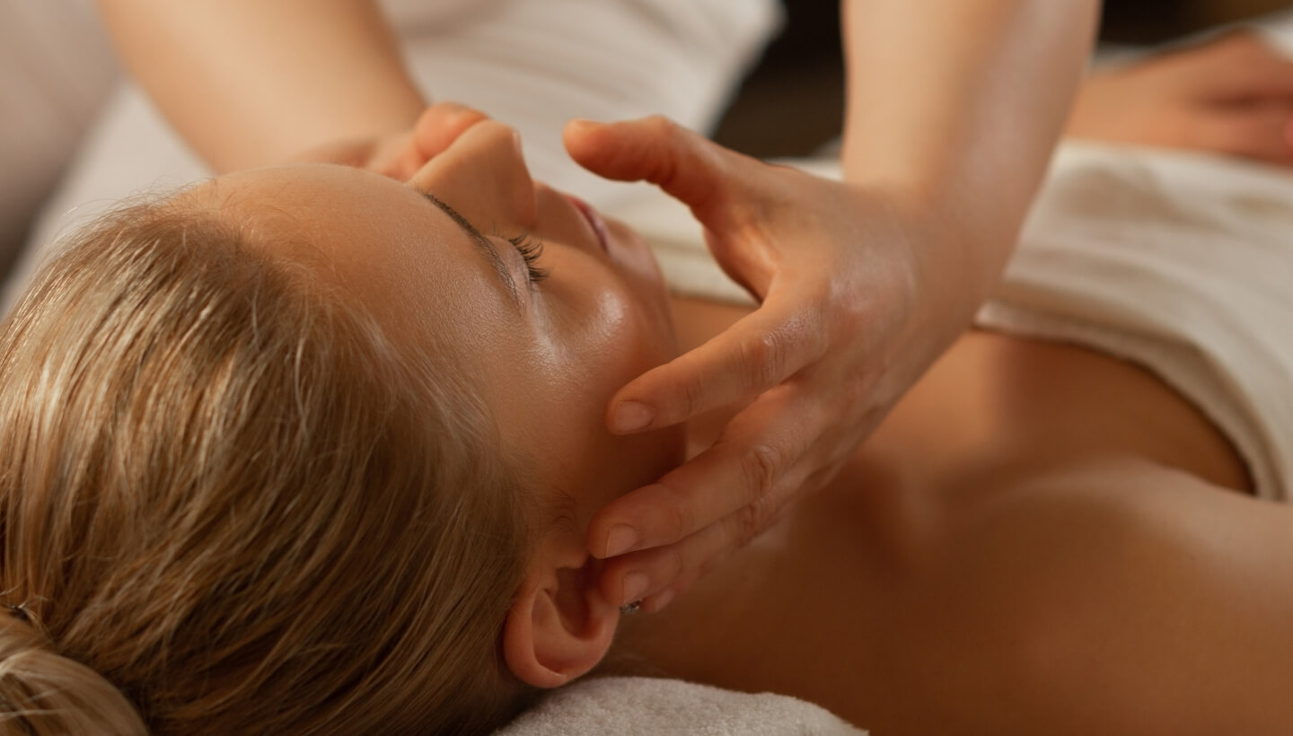 Persona con capelli biondi riceve un massaggio al viso, occhi chiusi.