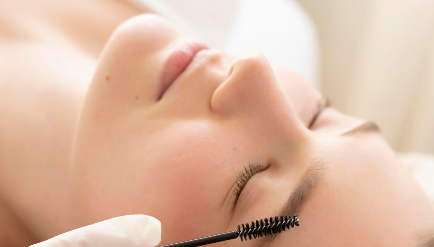 Close-up of a person with closed eyes, a brush near their eyebrow.   Primo piano di una persona con occhi chiusi, un pennello vicino al sopracciglio.