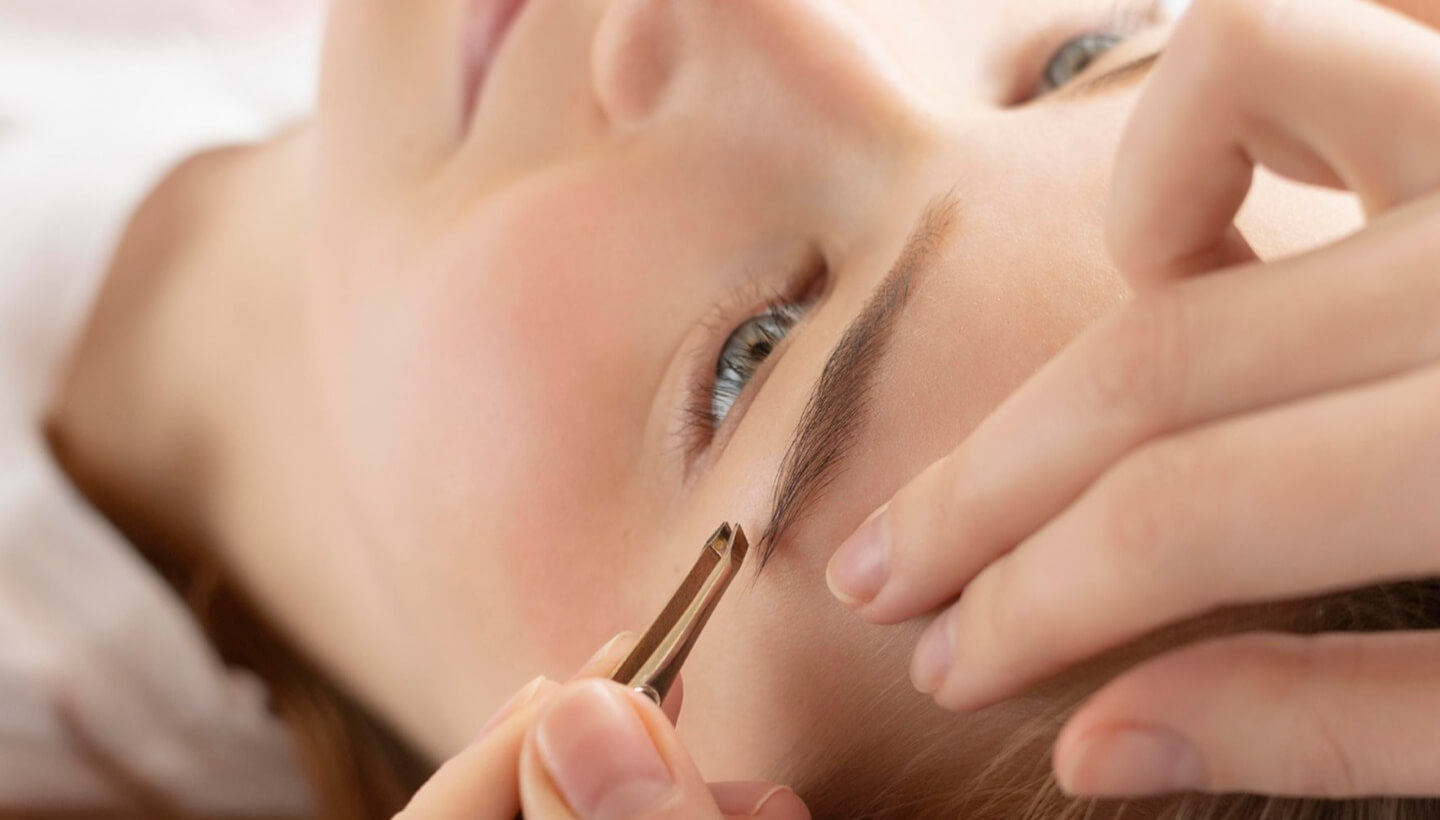 Close-up of a person shaping an eyebrow with tweezers.   Primo piano di una persona che modella un sopracciglio con pinzette.