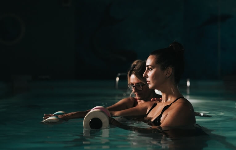 Due donne in piscina, una in costume nero e l'altra in rosso.