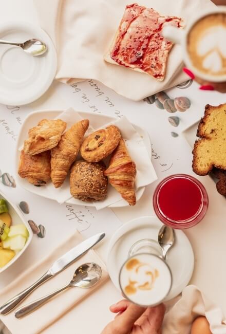 Colazione con pasticcini, toast, succo rosso e caffè con latte art.