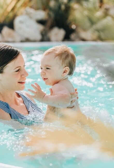Donna in costume a righe tiene un bambino in piscina.