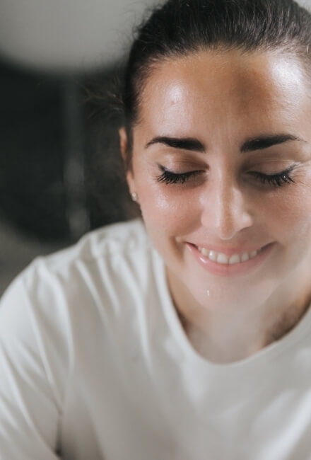 Donna con capelli scuri, t-shirt bianca, occhi chiusi e sorriso.