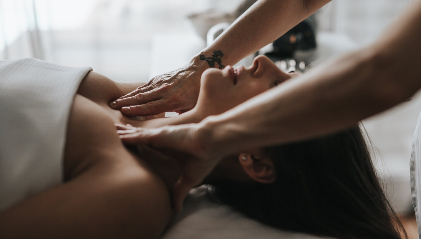 Donna su un tavolo da massaggio, due mani la massaggiano.