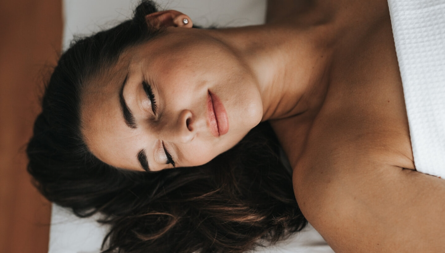 Donna sdraiata con gli occhi chiusi, coperta da un tessuto bianco.