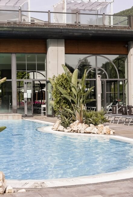 Piscina blu con sdraio, edificio con finestre e piante tropicali.