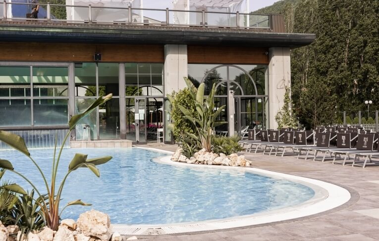 Piscina con lettini e tavoli, edificio con finestre sullo sfondo.