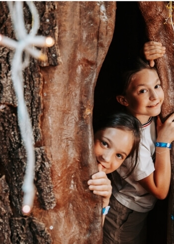 Due bambini si nascondono dietro tronchi con luci a stringa.