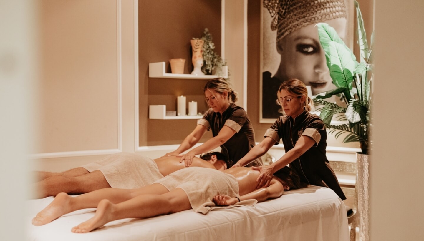 Two women massage individuals in a serene, decorated room.