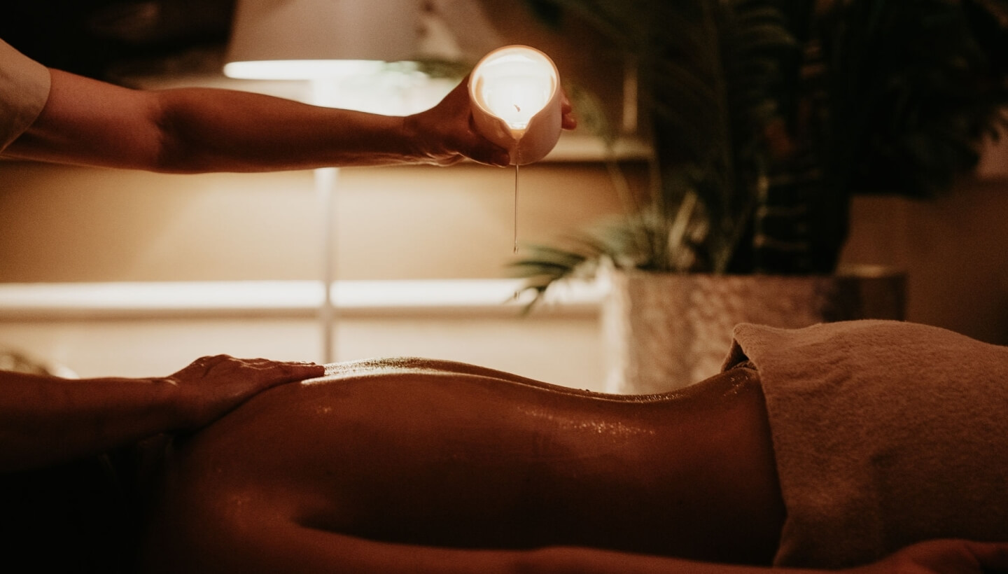 Persona che riceve un massaggio con olio caldo e candela accesa.