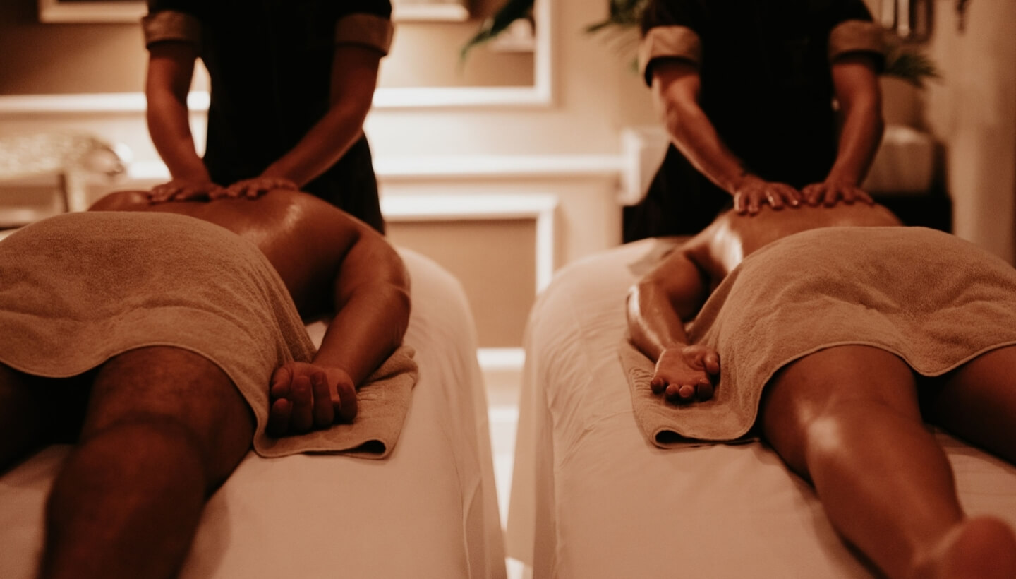 Zwei Personen erhalten Massagen in einem Spa-Raum mit Therapeuten.