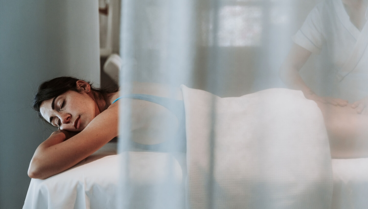 Woman receiving a massage on a table, partially obscured by a curtain.