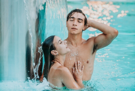 Due persone in piscina con una cascata d'acqua davanti.