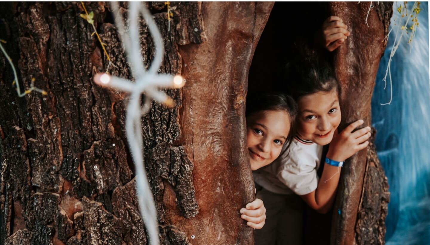 Due bambini si nascondono dietro un grande tronco d'albero.