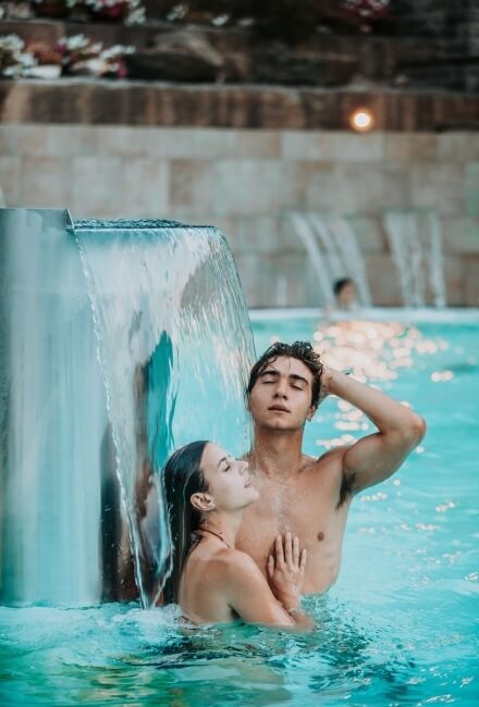 Uomo e donna in piscina con cascate sullo sfondo.