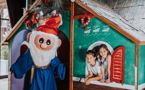 Costume di gnomo accanto a una casetta di legno decorata per Natale.