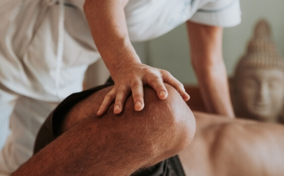 Eine Hand drückt auf ein Knie, im Hintergrund eine Buddha-Statue.